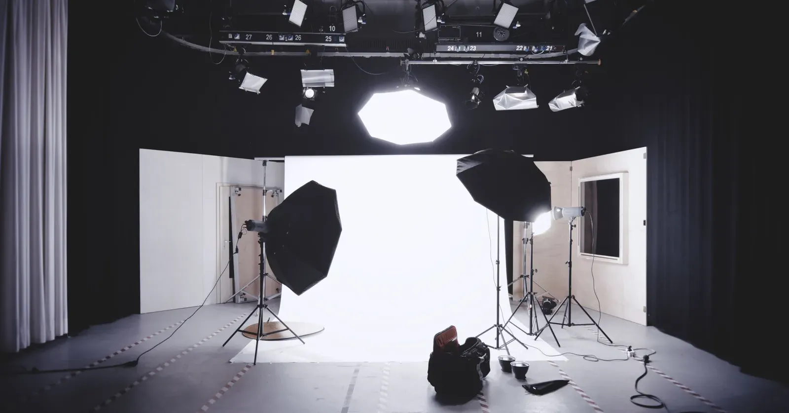สตูดิโอถ่ายภาพที่ยังว่าง มีฉากขาว ไฟร่มและซอฟต์บ็อกซ์หลายดวง และรางไฟบนเพดาน